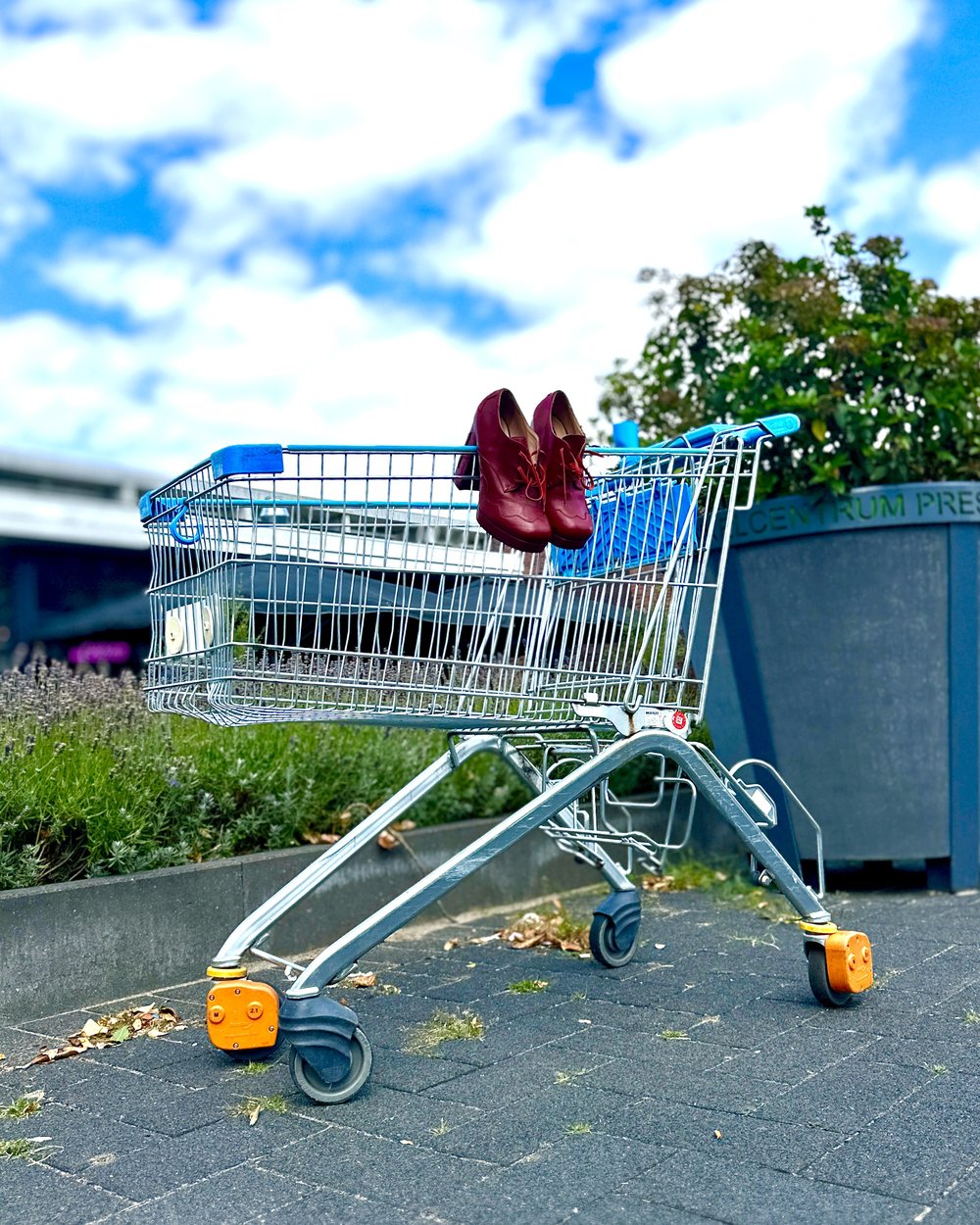 Een winkelwagen op straat met een paar donkerrode schoenen erin.